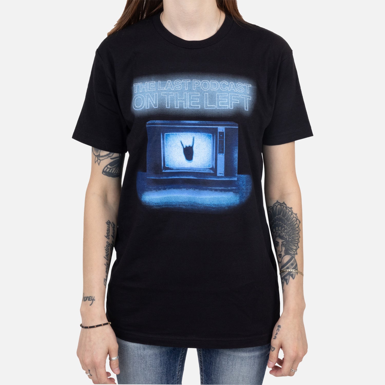 Female model wearing black tee with graphic of tv with hand making horns with text "THE LAST PODCAST ON THE LEFT"