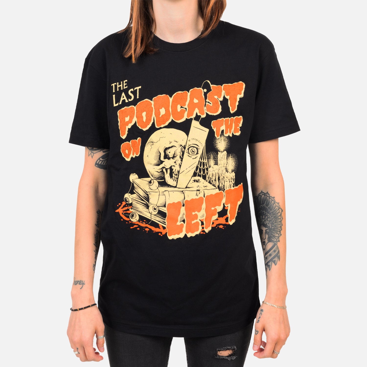 black tee on female model with THE LAST PODCAST ON THE LEFT logo featuring skull knife and books and candle graphic