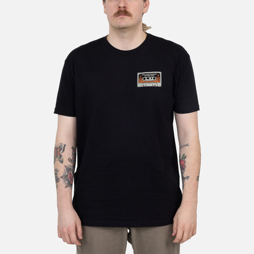 Black shirt with cassette graphic on left chest with text "THE LAST PODCAST ON THE LEFT"