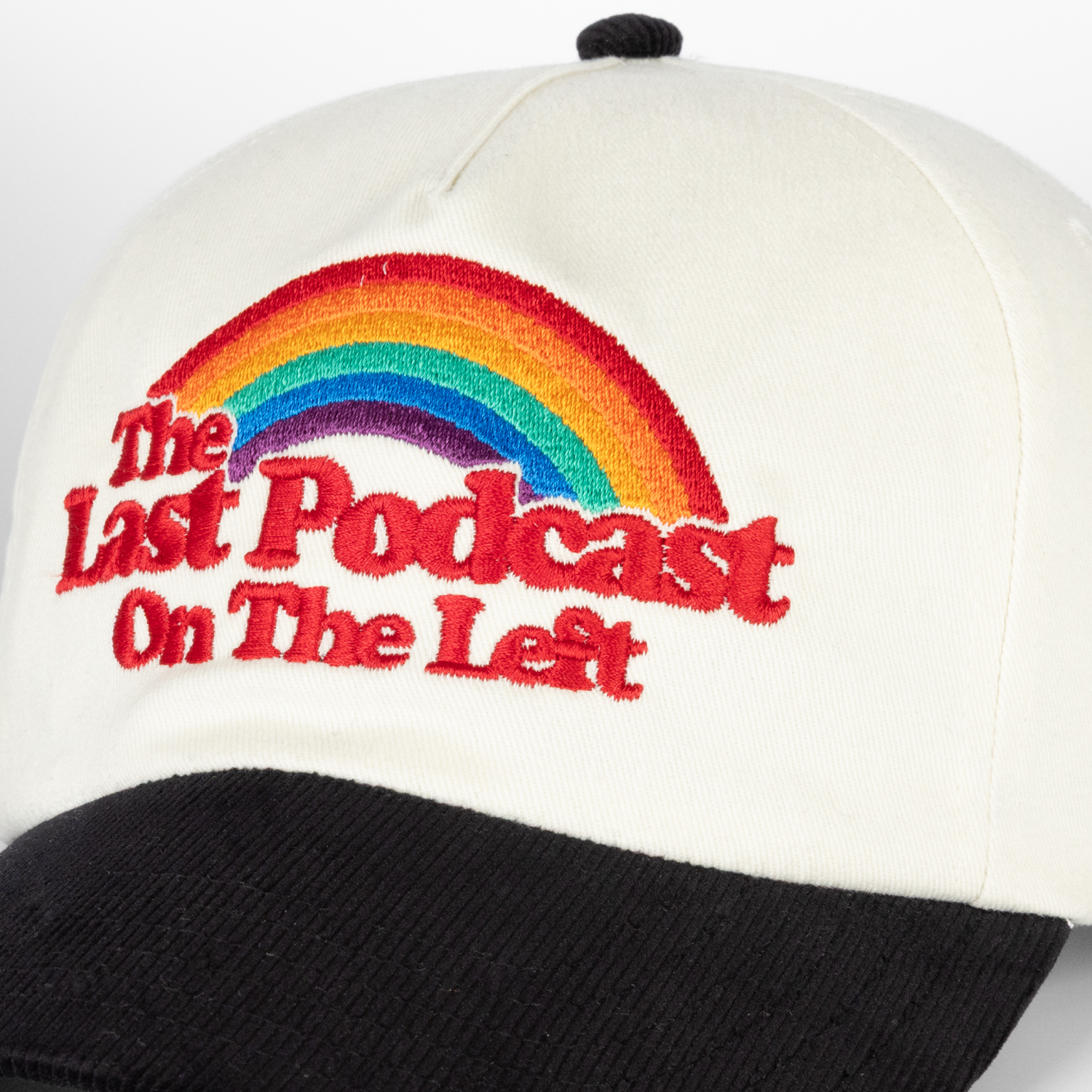Closeup of cream and black hat with rainbow on front with text "The Last Podcast On The Left"