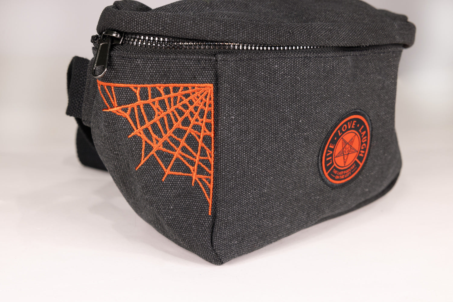 Closeup of Black Fanny pack with orange  pentagram "LIVE LOVE LAUGH" patch on front with orange spider webs on sides