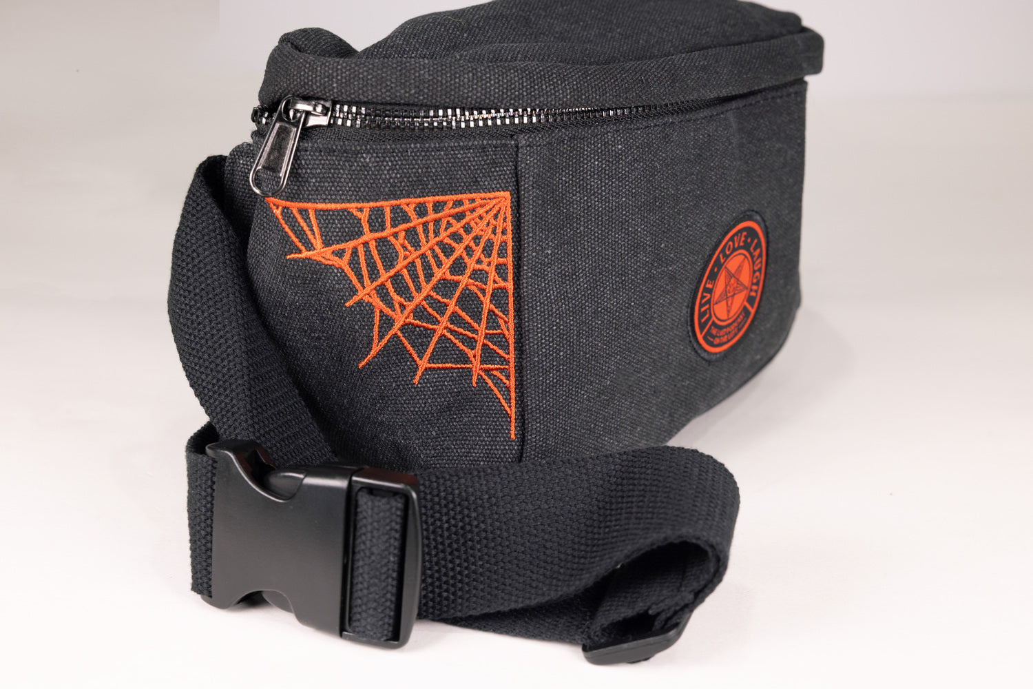 closeup of Black Fanny pack with orange  pentagram "LIVE LOVE LAUGH" patch on front with orange spider webs on sides showing strap