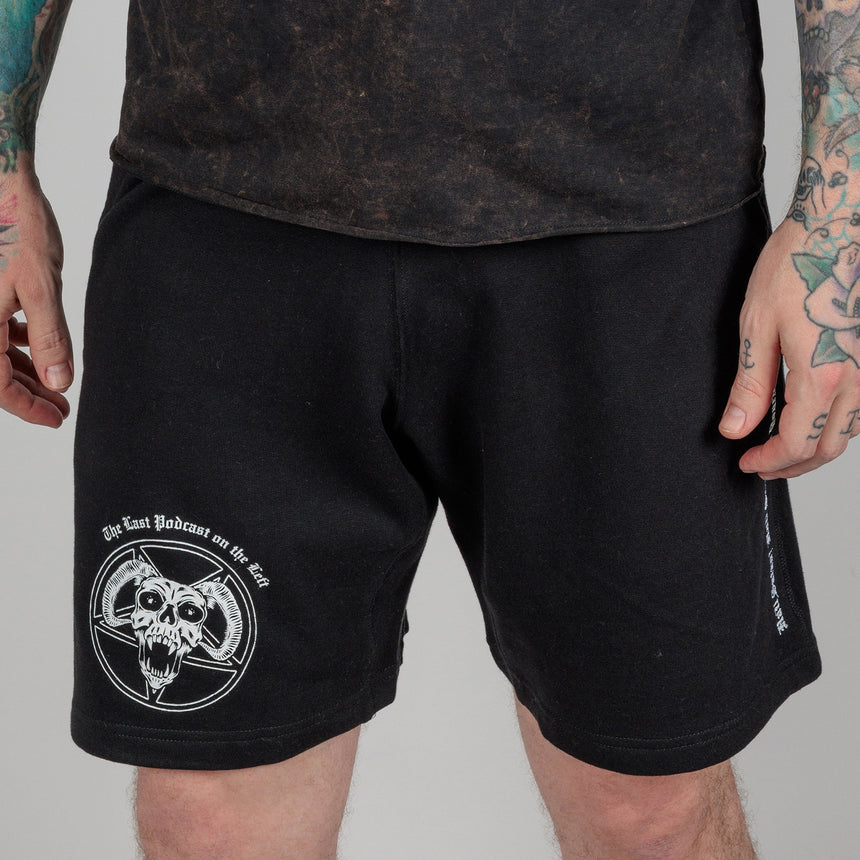 photo of male model wearing demon's head sweatshort in black. inverted pentagram with horned skull in foreground on right leg above knee. "the last podcast on the left printed above.