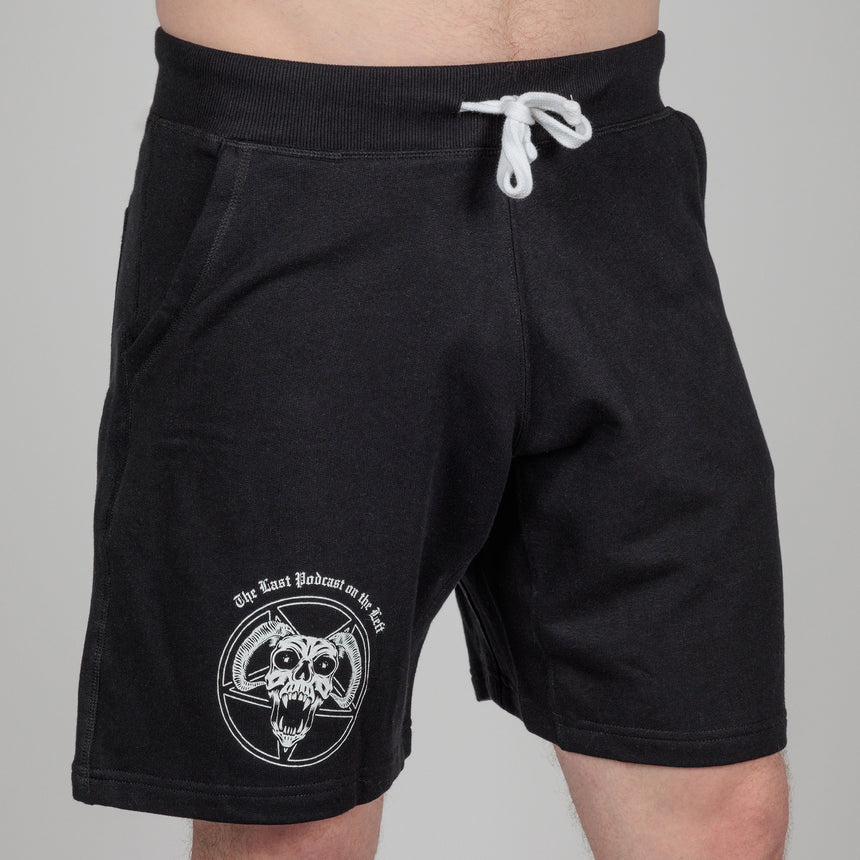 photo of male model wearing demon's head sweatshort in black. inverted pentagram with horned skull in foreground on right leg above knee. "the last podcast on the left printed above.
