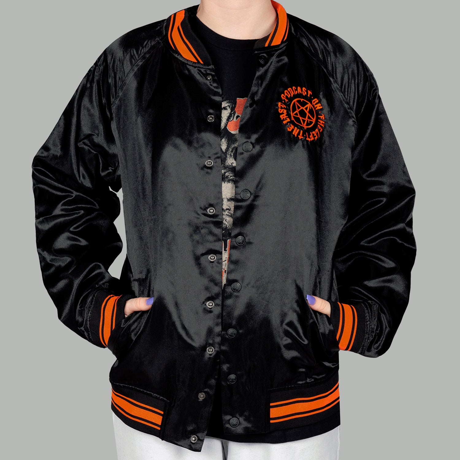 woman in black satin jacket with orange pentagram on left chest with text "THE LAST PODCAST ON THE LEFT"