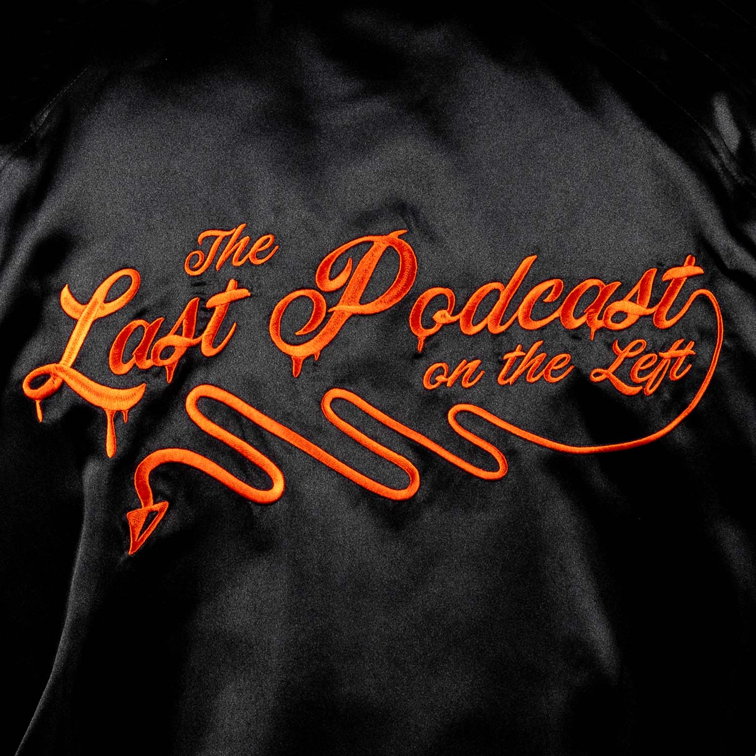 closeup of back of satin jacket showing orange text "The Last Podcast on the Left"