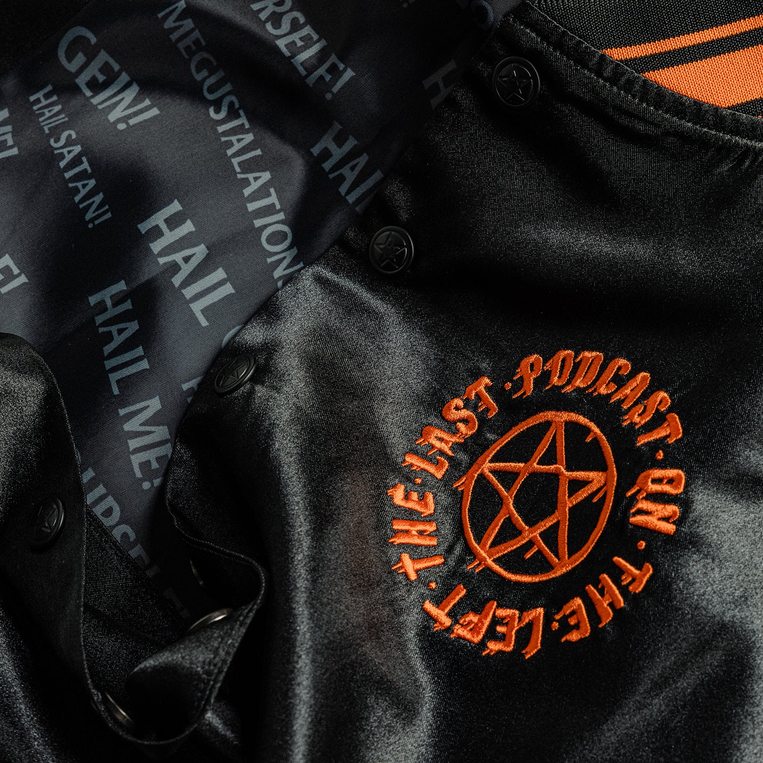 closeup of front left of black satin jacket showing orange pentagram with text "THE LAST PODCAST ON THE LEFT" and closeup of interior with various text "HAIL SATAN! HAIL ME! HAIL GEIN! MEGUSTALATIONS HAIL YOURSELF!"