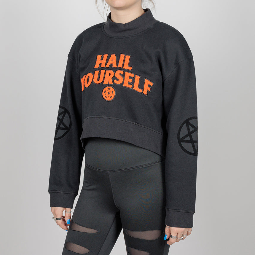 woman in black cropped sweatshirt with orange "Hail Yourself" text and pentagram