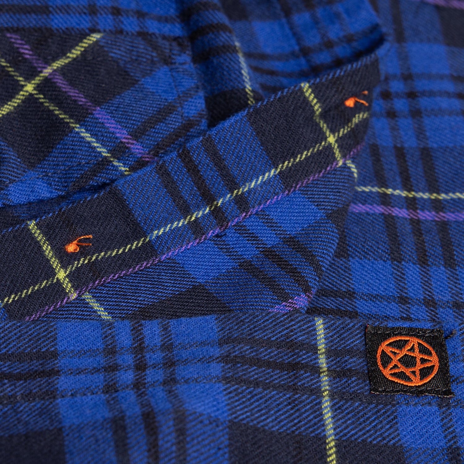 closeup of black label on blue plaid flannel buttondown with orange pentagram