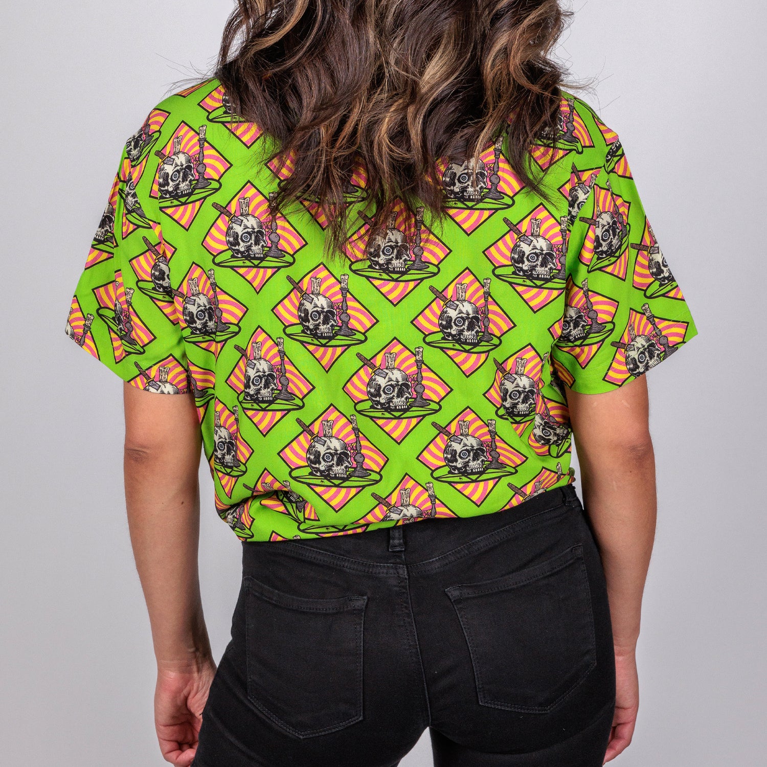 rear view photo of female model wearing occult altar short sleeve buttondown. acid green background with skull on plate on orange background.