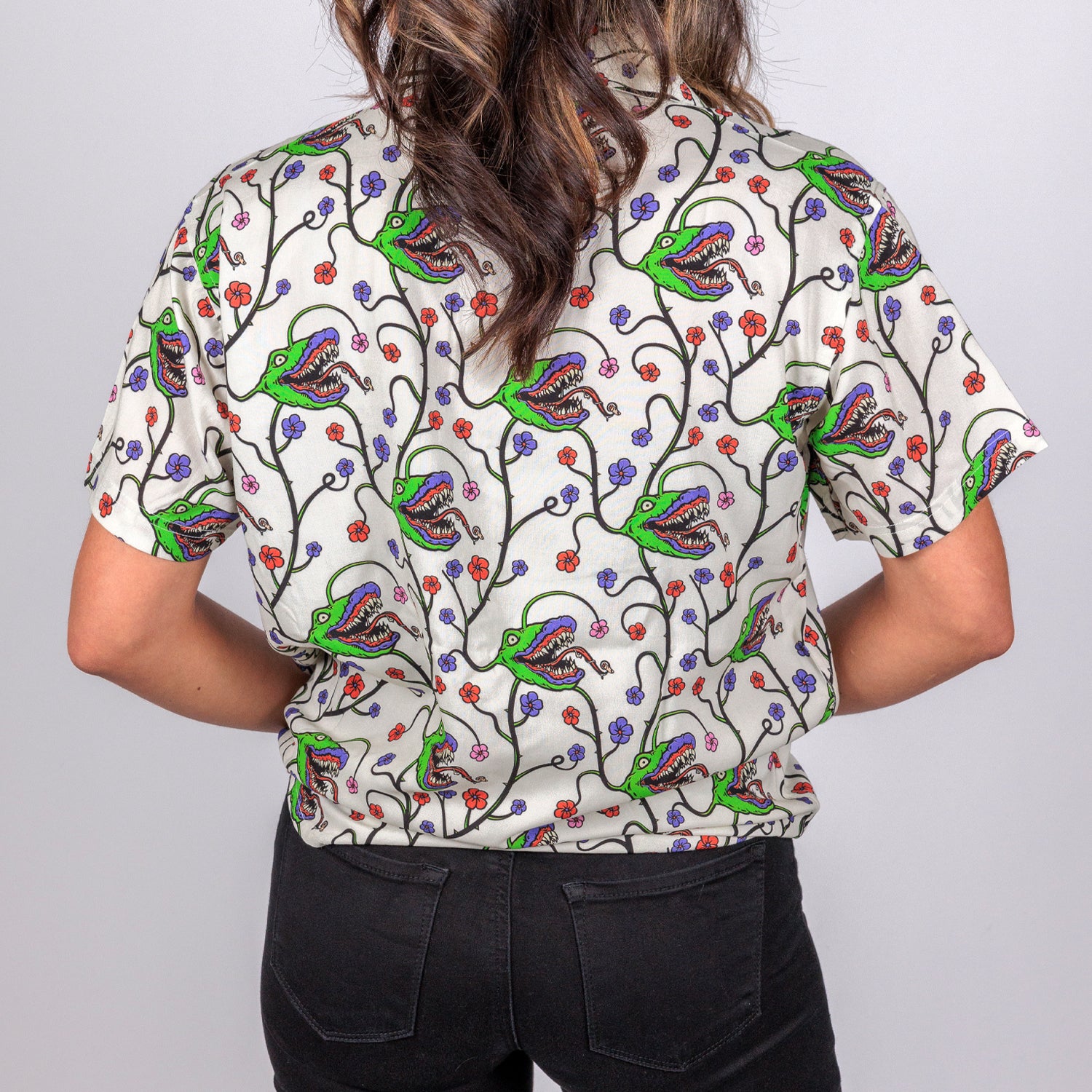 rear view photo of female model wearing man-eating plant short sleeve buttondown in bone color. pattern of man eating plant