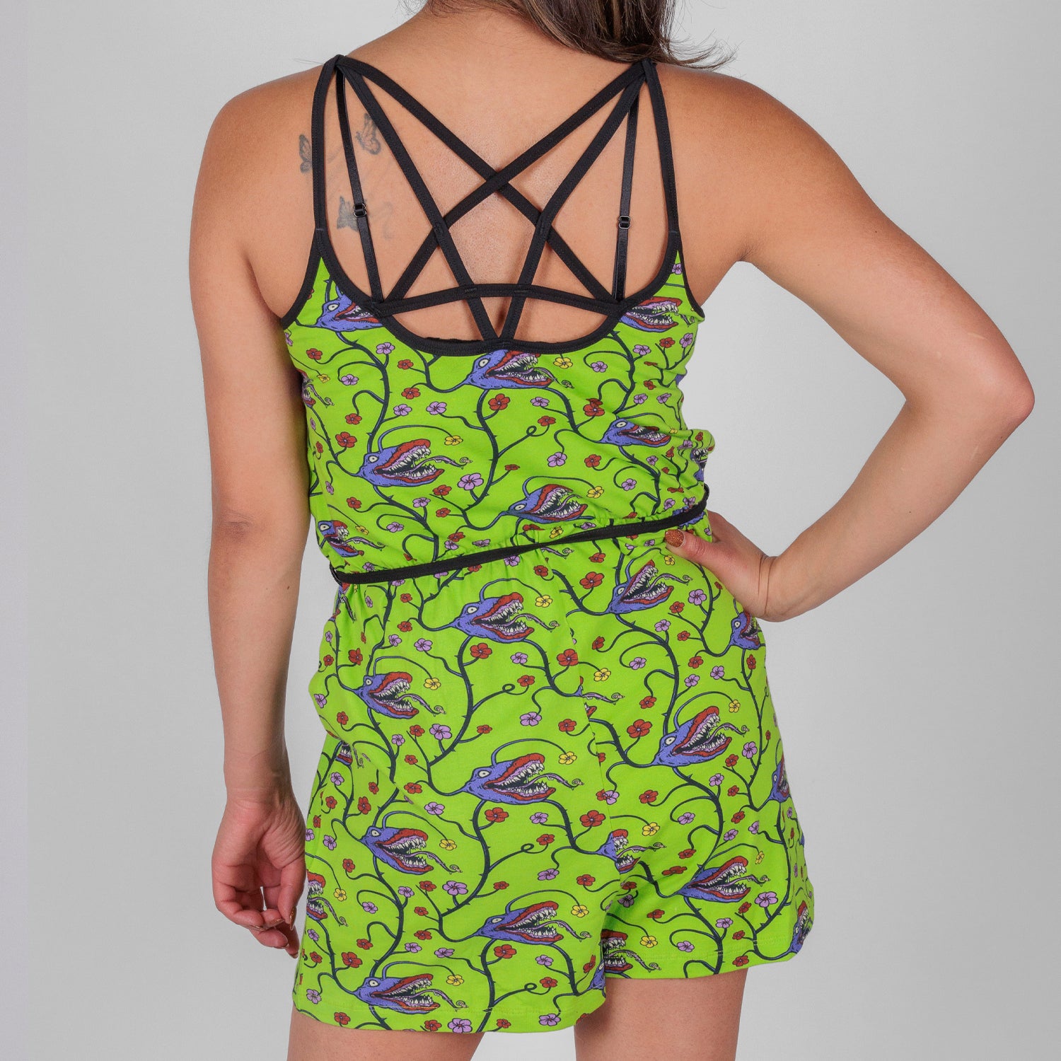 rear photo of female model wearing short romper with man eating plant pattern on acid green background