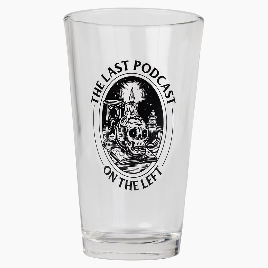 Pint glass with black graphic on side of skull with lit candle on top and sitting on a book next to hour glass surrounded by text "THE LAST PODCAST ON THE LEFT"