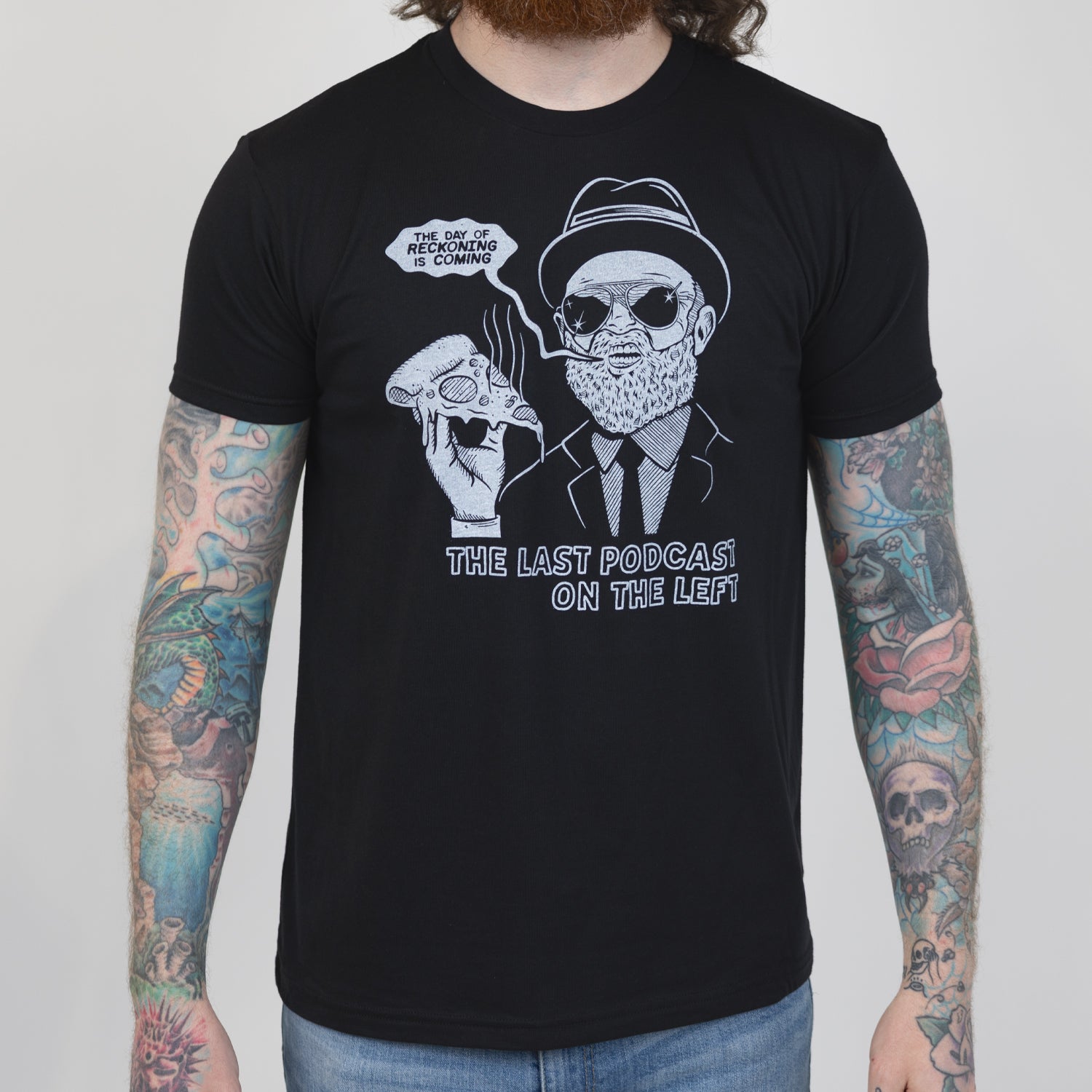 Man in black shirt with graphic of man in suit and hat holding pizza with speech bubble "THE DAY OF RECKONING IS COMING" and text below "THE LAST PODCAST ON THE LEFT"