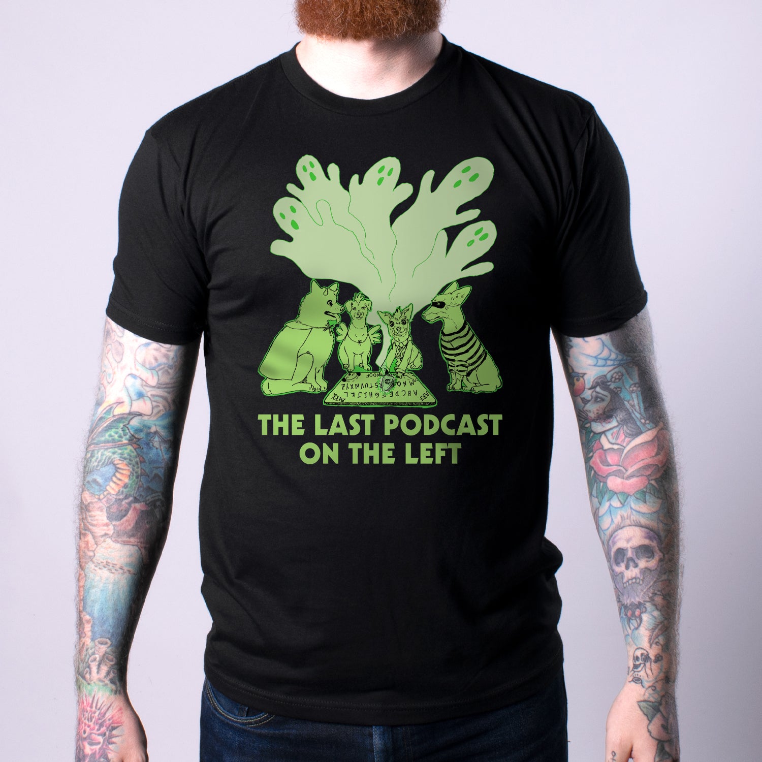 man in black Shirt with green graphic of dogs performing a seance, with green text below "THE LAST PODCAST ON THE LEFT"